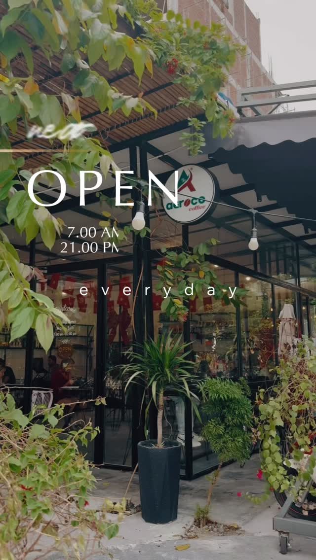 Bảng “OPEN” treo trước mặt tiền kính đầy cây xanh của Aeroco