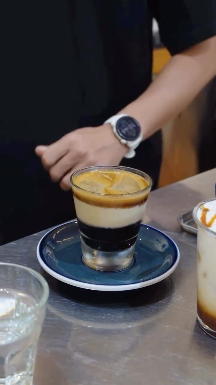 A barista's wrist mid-pour, spring decor in frame