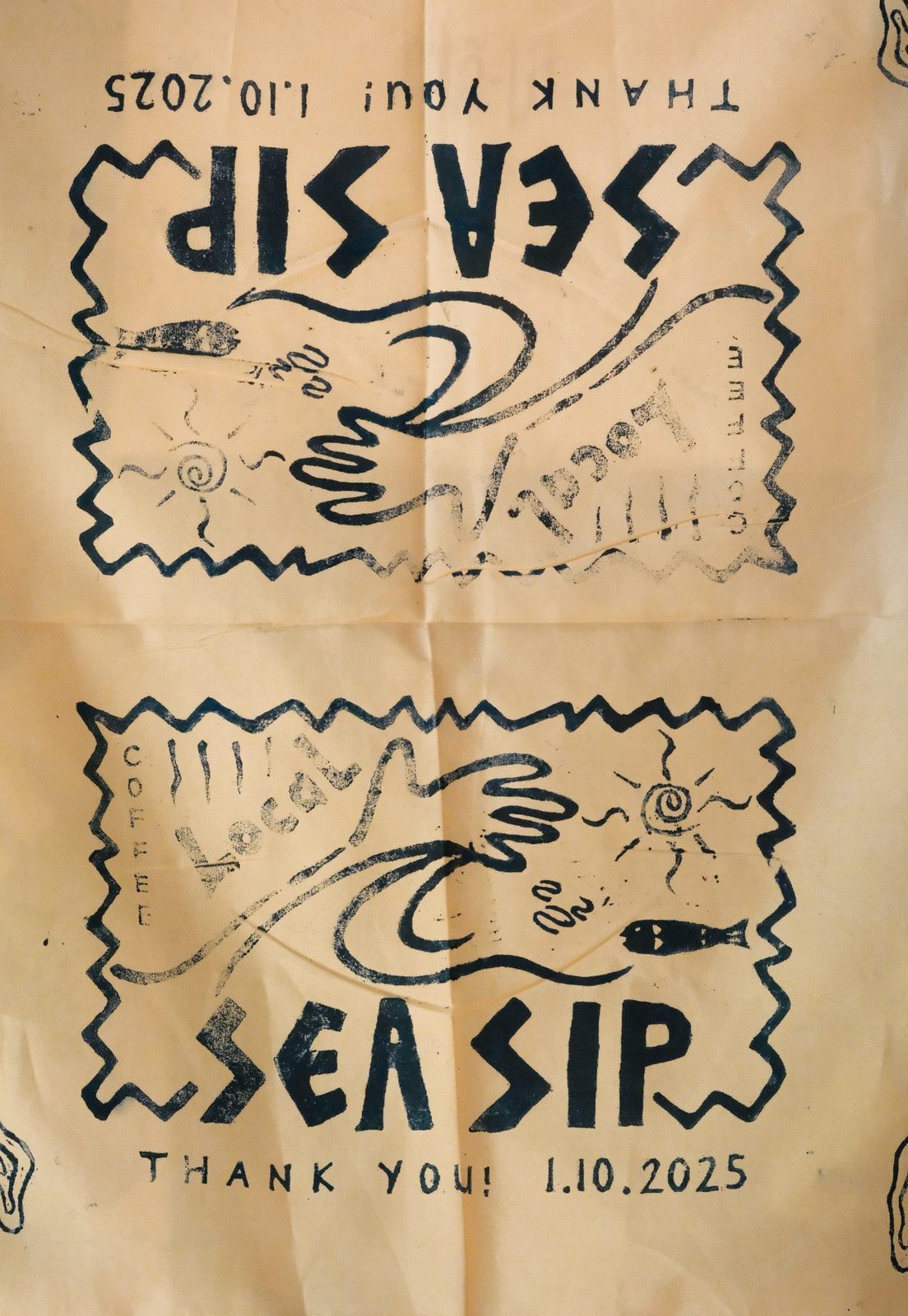 A hand block-printed banner with 'Sea Sip' lettering and wave, sun and fish motifs