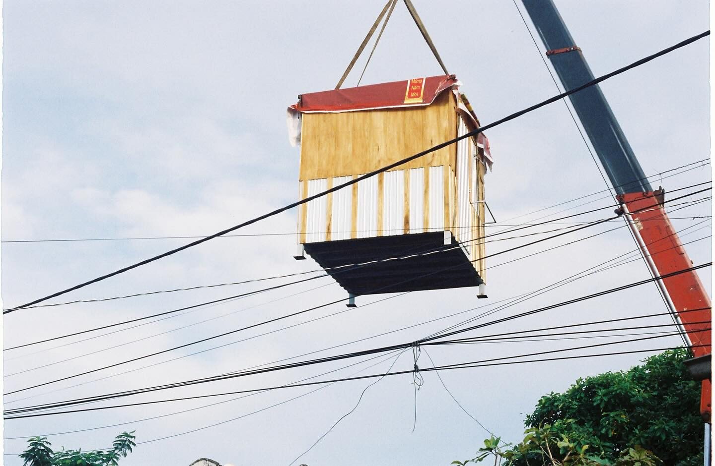 The finished mobile wooden cabin, suspended from a crane hook mid-delivery