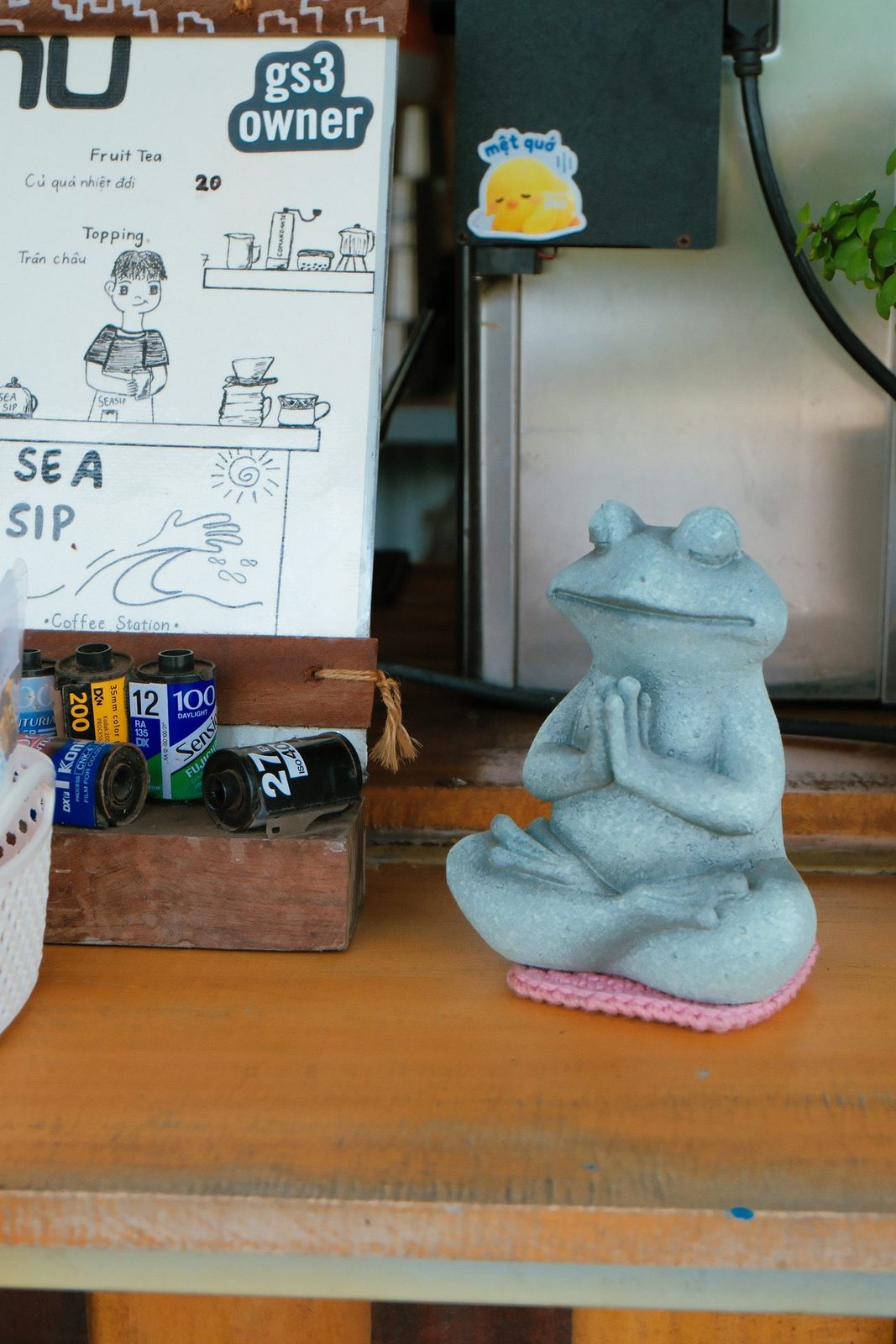 A meditating frog figurine beside a hand-drawn menu board and film rolls
