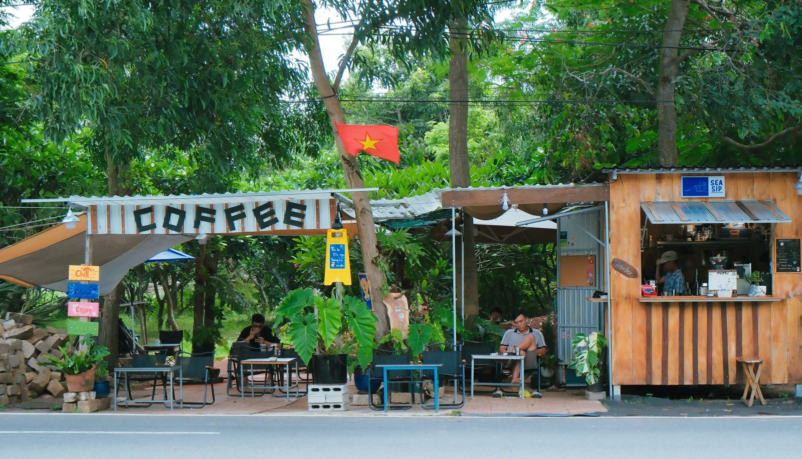 A wide view of the kiosk roadside under the trees, with guests seated over their coffee