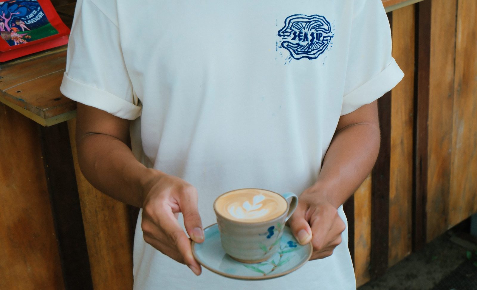 A barista holding a latte-art cup, wearing a Sea Sip logo tee